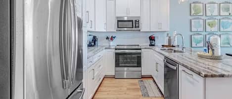Kitchen features a refrigerator, microwave, oven, and dishwasher, along with a sink and wooden floor.