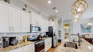 A modern kitchen with white cabinets, stainless steel appliances, granite countertops, and a unique geometric pendant light.