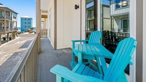 A balcony with two turquoise Adirondack chairs, a glass door, and a view of the beach and other buildings.