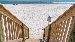 A wooden staircase leading to a beach with a sign indicating a 100 ft. distance to the water.