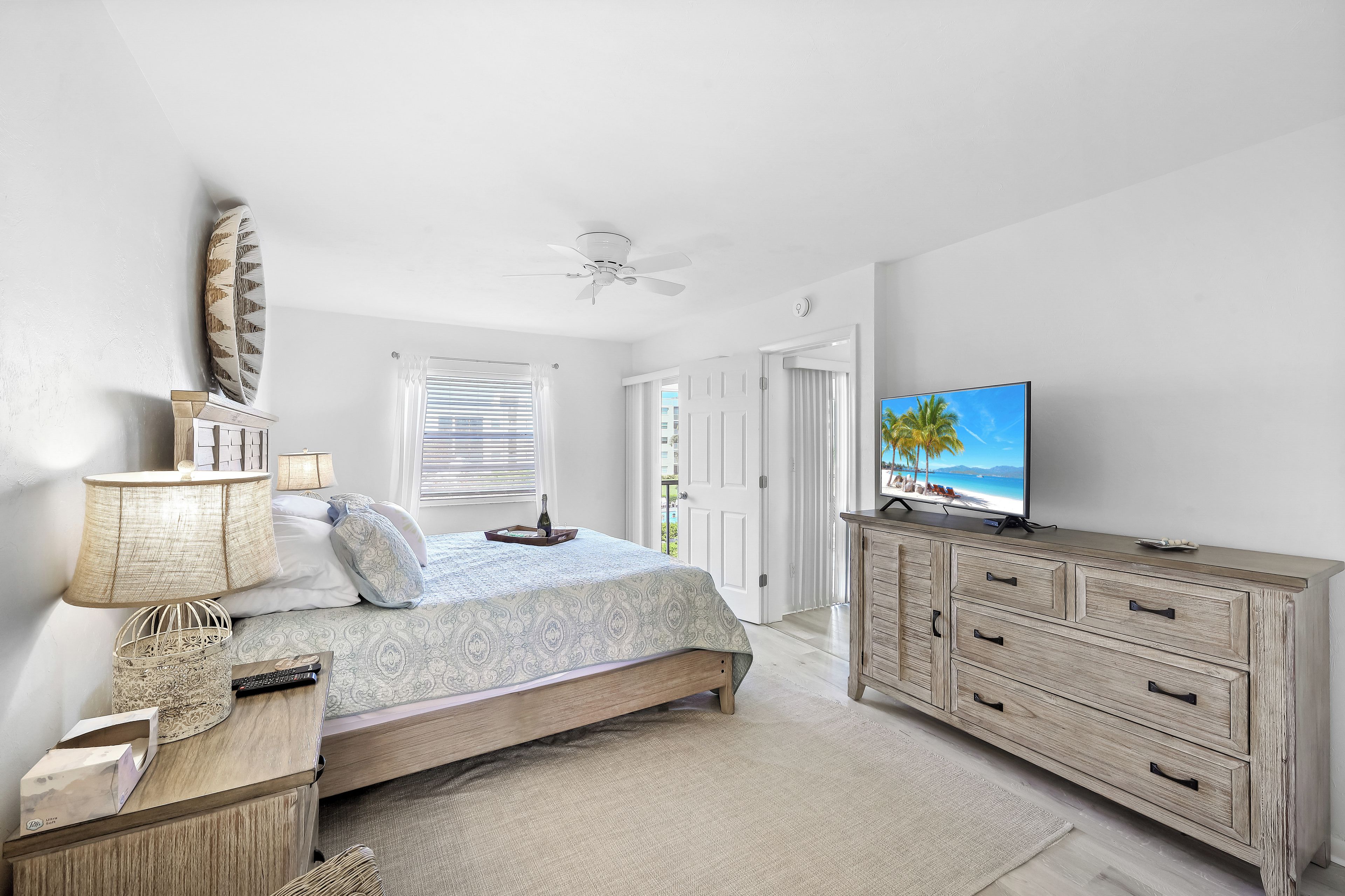 A bedroom with a bed, bedside table, lamp, TV, and a dresser.