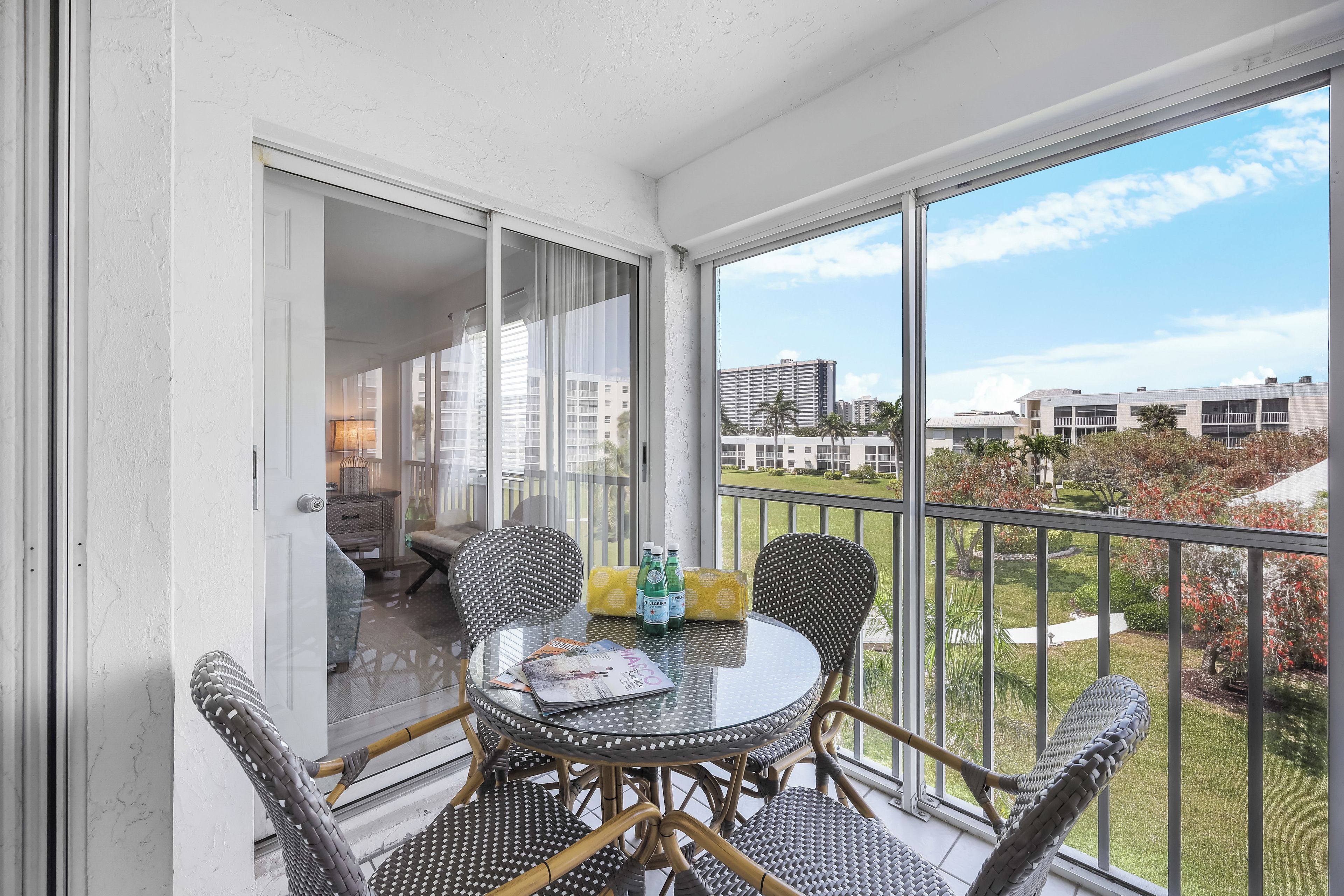 A balcony with wicker chairs, a glass table, and bottles.