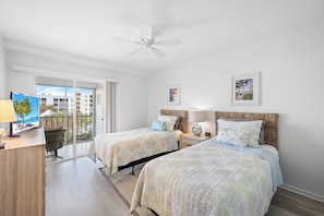 A hotel room with two beds, a desk, a chair, a ceiling fan, and a view of the outside. - Coastal Condo | Short Walk Away From the Beach (Marco Island)