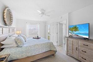 A bedroom with a bed, a television, a ceiling fan, and a view of the outdoors.