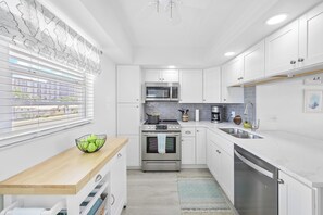 A modern kitchen with white cabinets, stainless steel appliances, and a wooden countertop. - Coastal Condo | Short Walk Away From the Beach (Marco Island)