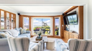 A spacious living room with a large window, a sofa, a coffee table, and a TV mounted on the wall. - Paradise Awaits you!  Sleeping 14, this oceanfront complex is perfect! (Dennis Port)