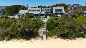 A beachfront property with a wooden staircase leading to a house, surrounded by dense greenery and sandy beach. - Paradise Awaits you!  Sleeping 14, this oceanfront complex is perfect! (Dennis Port)