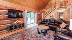 Un intérieur en bois avec une grande télévision, un canapé en cuir et un escalier.