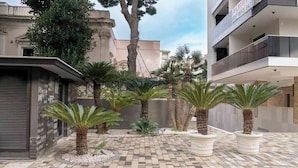 A courtyard with palm trees, a tiled floor, and modern buildings in the background. - Malcangi 29 (Trani)