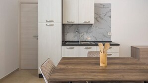 A modern kitchen with white cabinets, a marble backsplash, and a wooden dining table with a utensil holder. - Malcangi 29 (Trani)