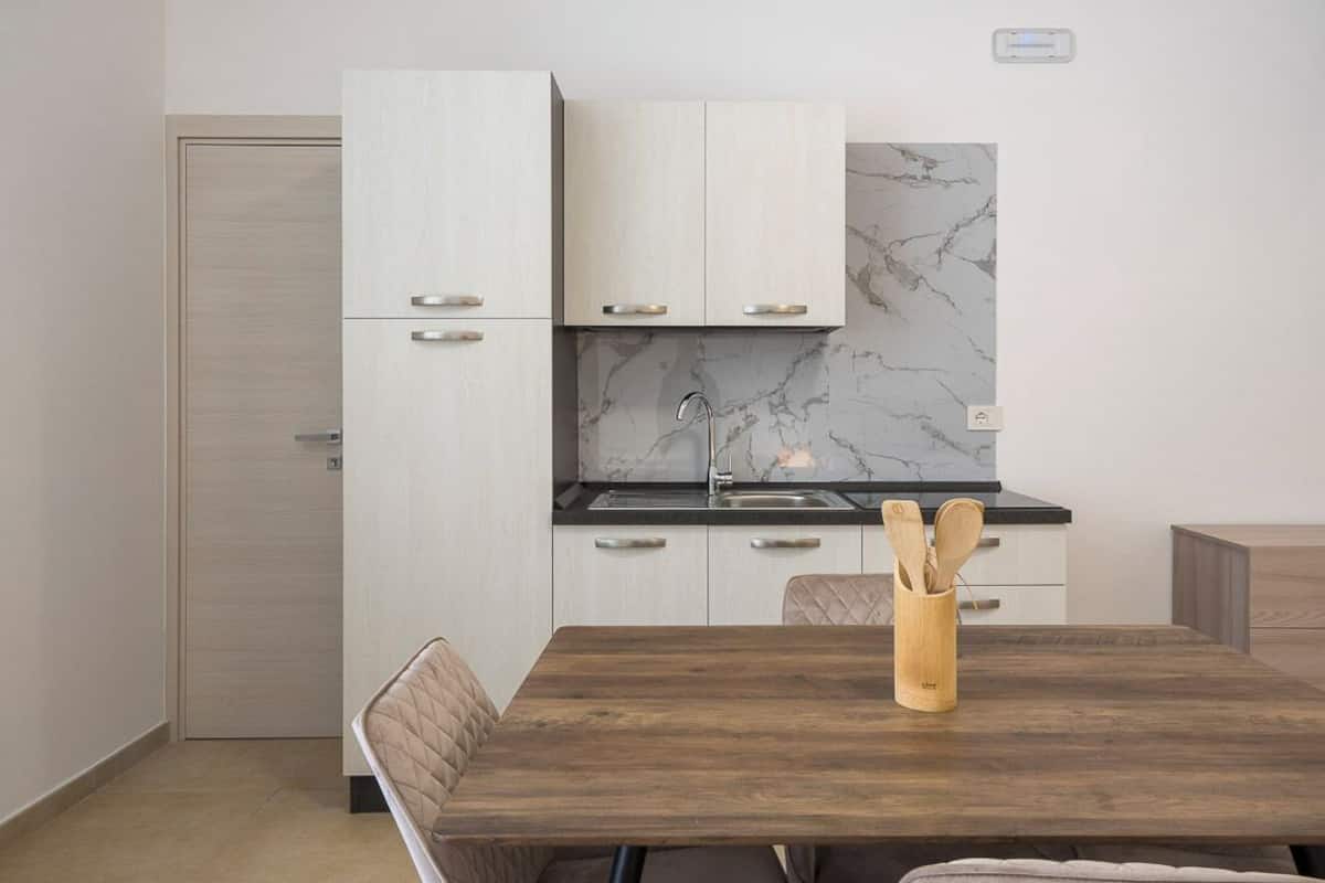 A modern kitchen with white cabinets, a marble backsplash, and a wooden dining table with a utensil holder.