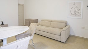 A minimalist living room with a beige sofa, a round dining table, and a single chair. - Malcangi 29 (Trani)