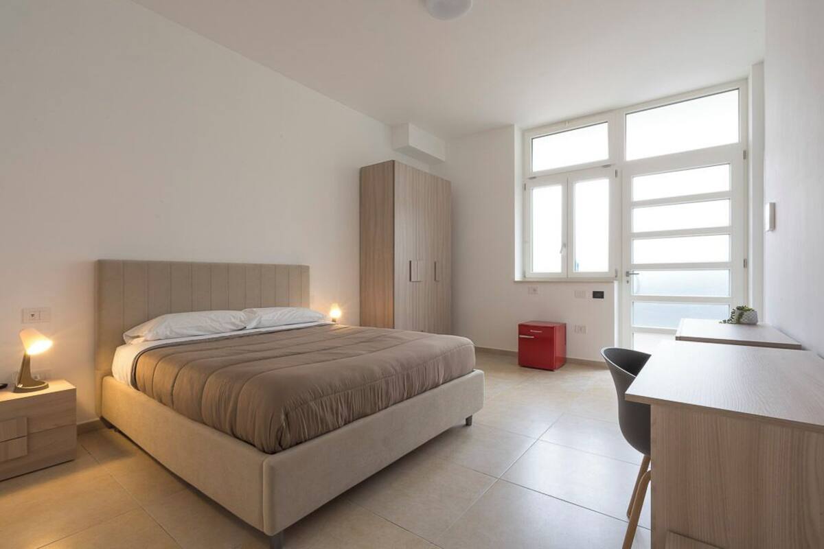 A modern bedroom with a bed, bedside tables, a desk, and a window.