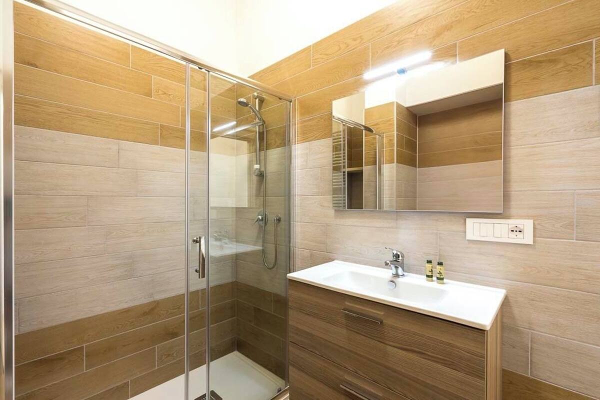 A modern bathroom with a glass shower enclosure, a wooden vanity, and a mirror above the sink.