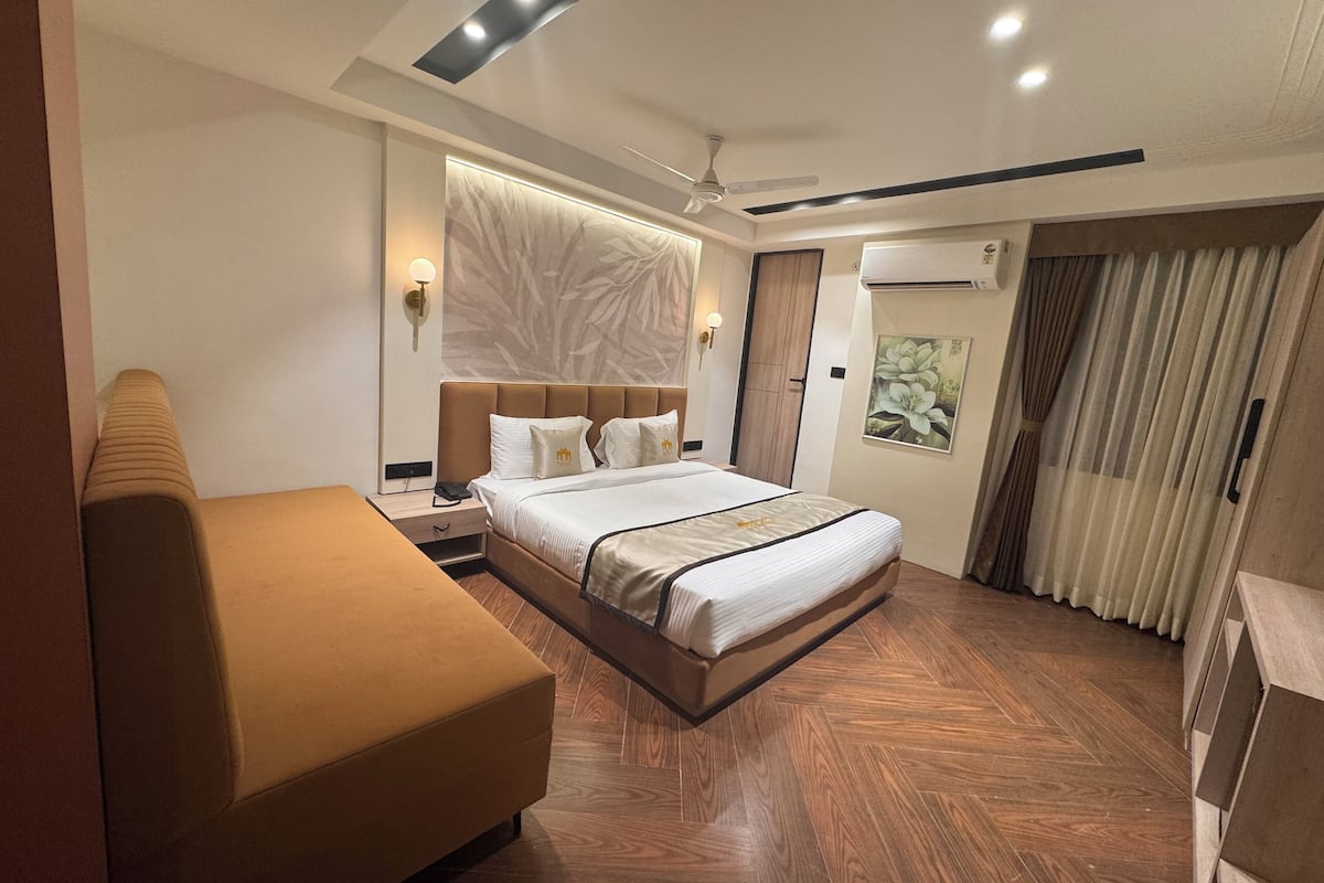 A modern hotel room with a large bed, a sofa, a bedside table, and a ceiling fan.