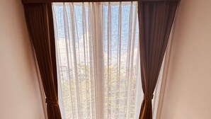 A corner room with a wooden floor, a round table, an orange chair, and a view through sheer curtains.