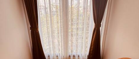 Habitación de esquina con piso de madera, una mesa redonda, una silla naranja y vistas a través de cortinas traslúcidas.