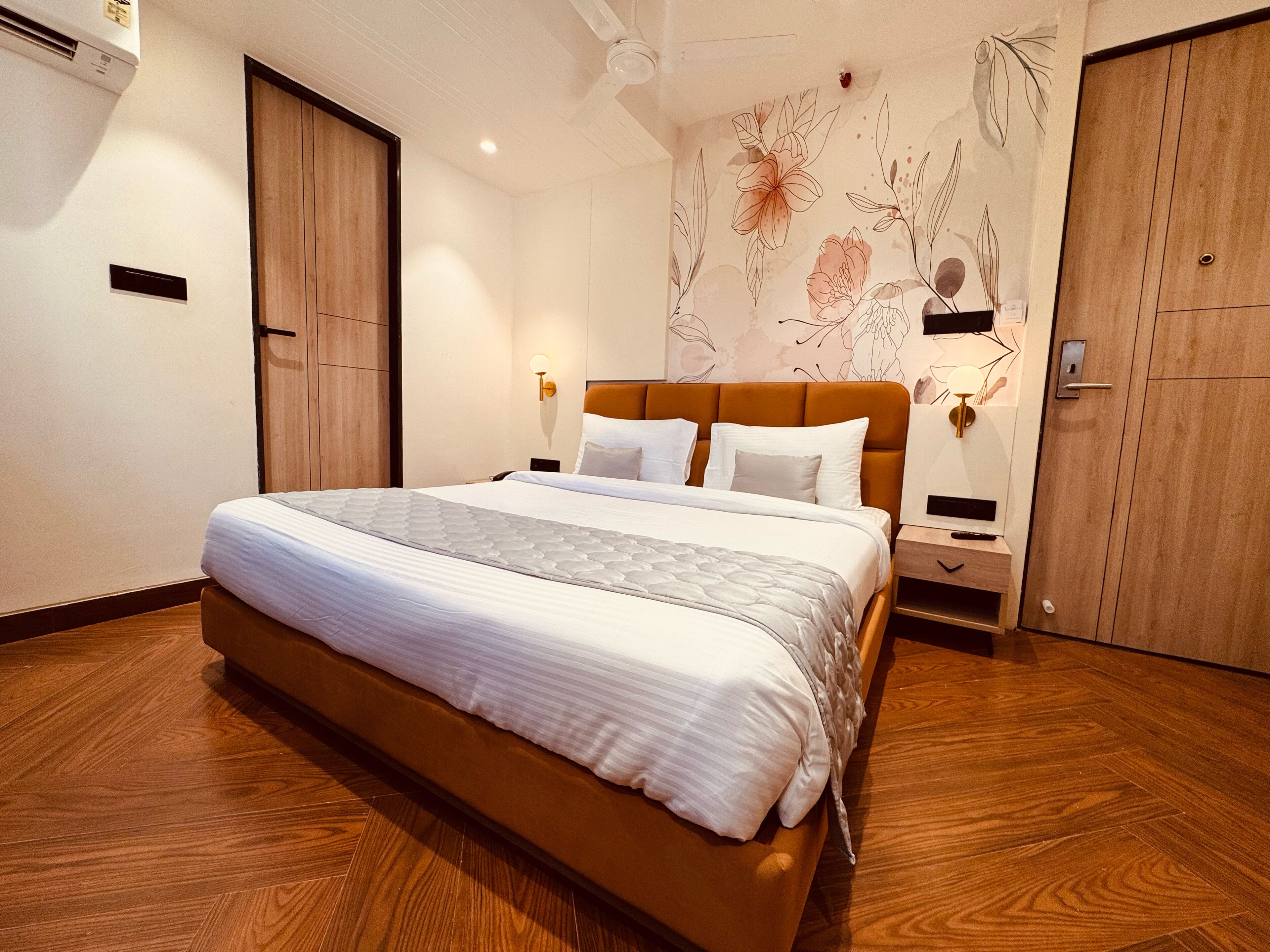 A modern hotel room with a large bed, wooden floor, and a floral wall mural.
