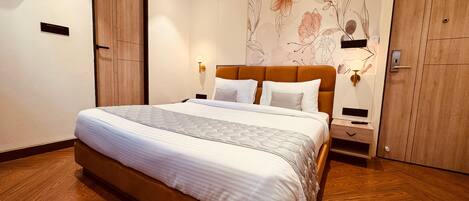 A modern hotel room with a large bed, wooden floor, and a floral wall mural.