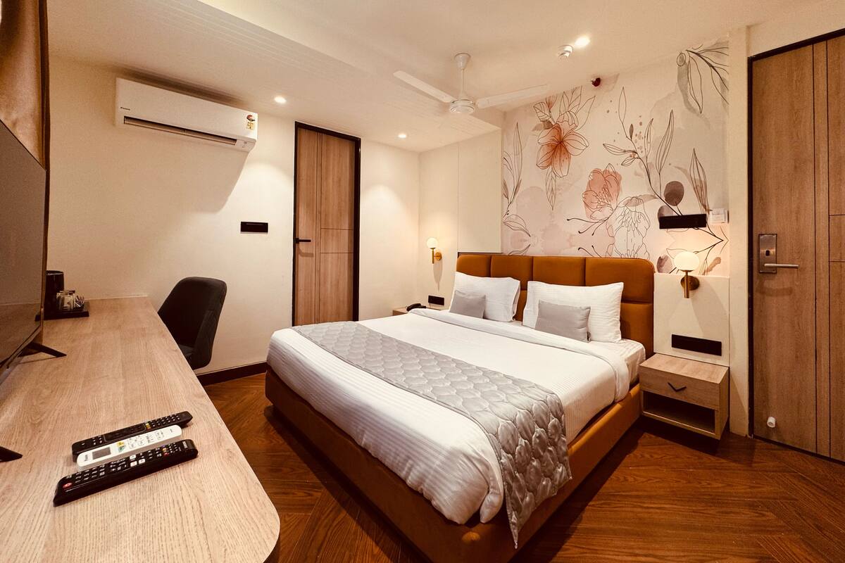 A hotel room with a bed, bedside tables, a desk with a chair, a TV, and a wardrobe.