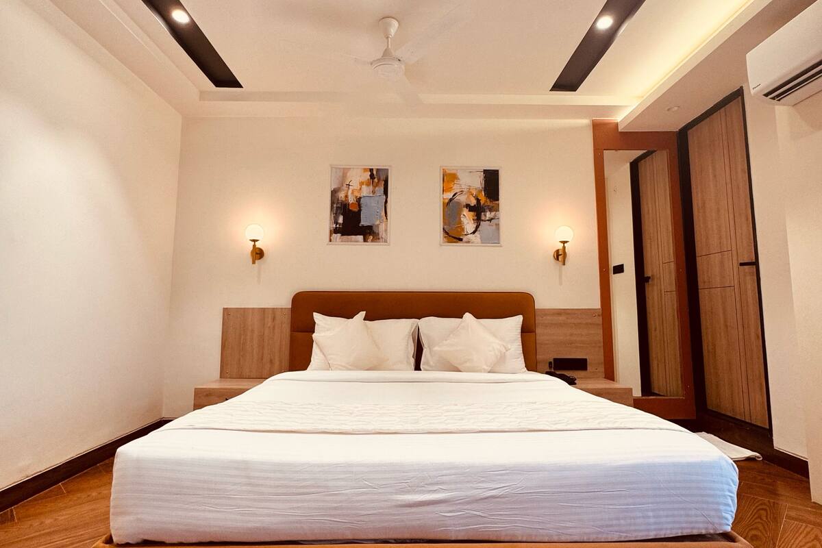 A bedroom with a large bed, wooden flooring, a ceiling fan, and two wall-mounted light fixtures.