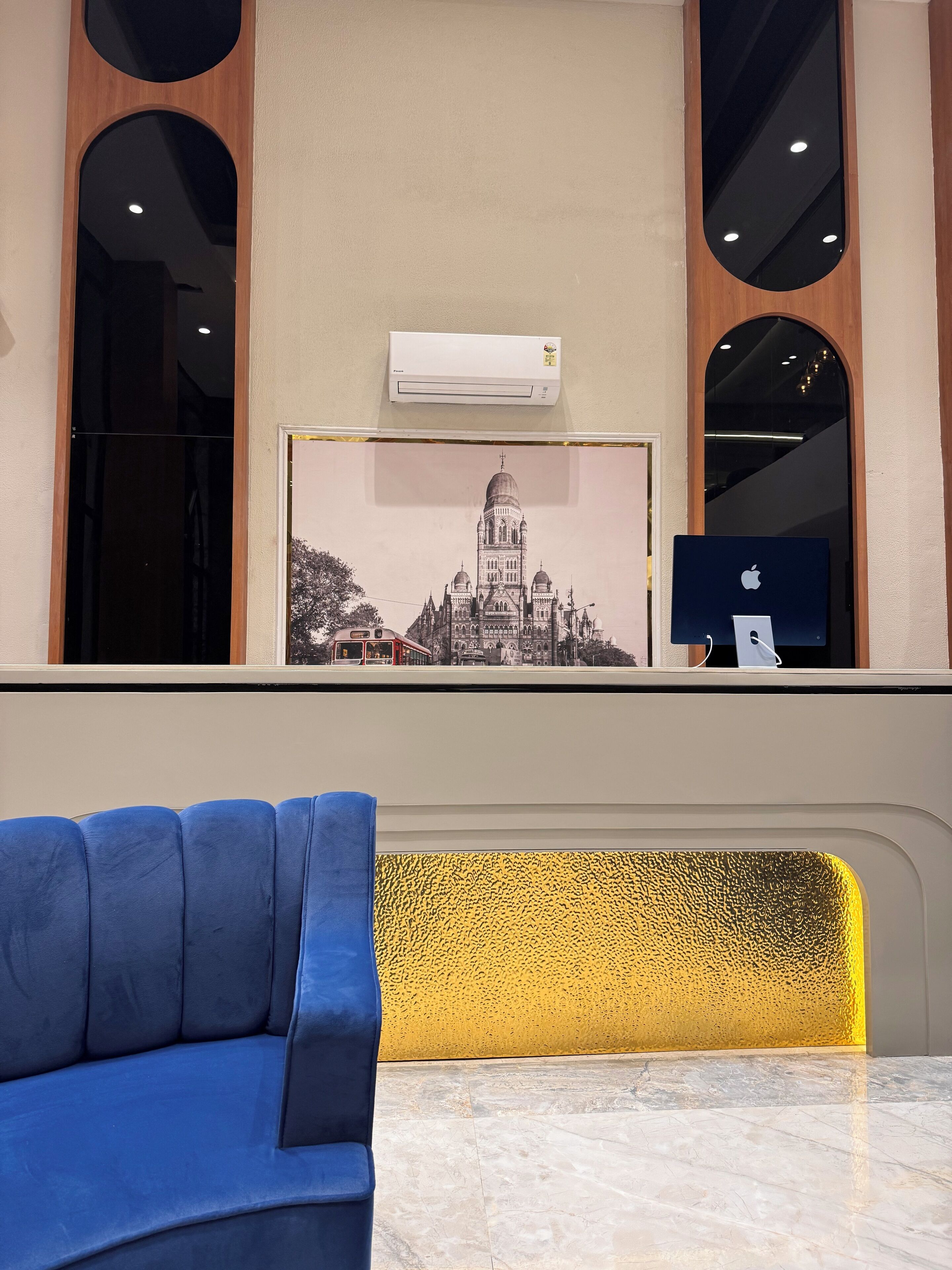 A reception desk with a framed cityscape picture, an air conditioning unit, and a blue sofa in the foreground.