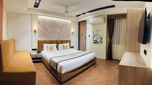 A hotel room with a large bed, a bedside table with a lamp, a ceiling fan, an air conditioning unit, and a painting on the wall.