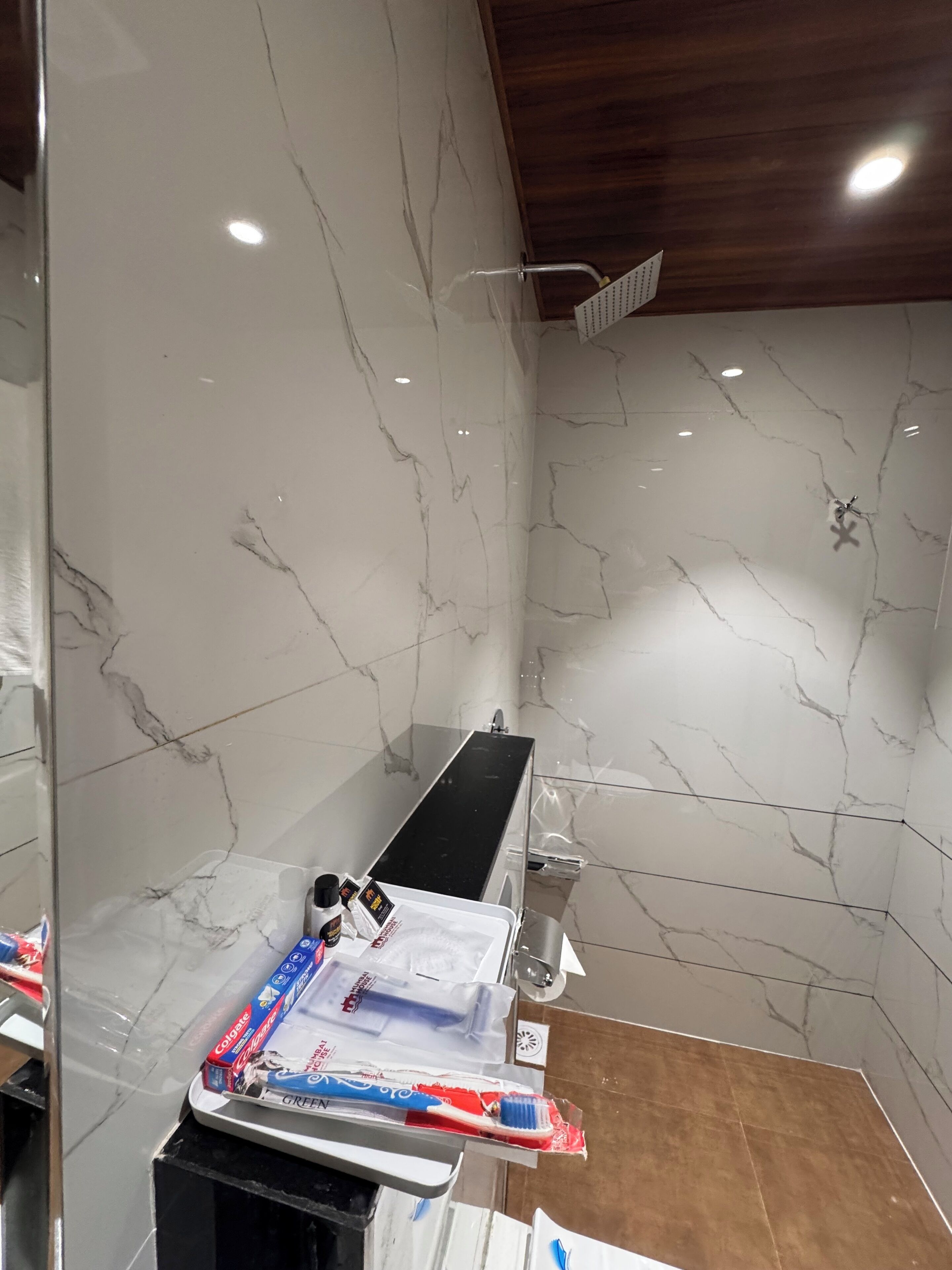 A bathroom with a marble wall, a black countertop, and a shower area.