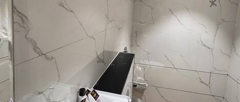 A bathroom with a marble wall, a black countertop, and a shower area.
