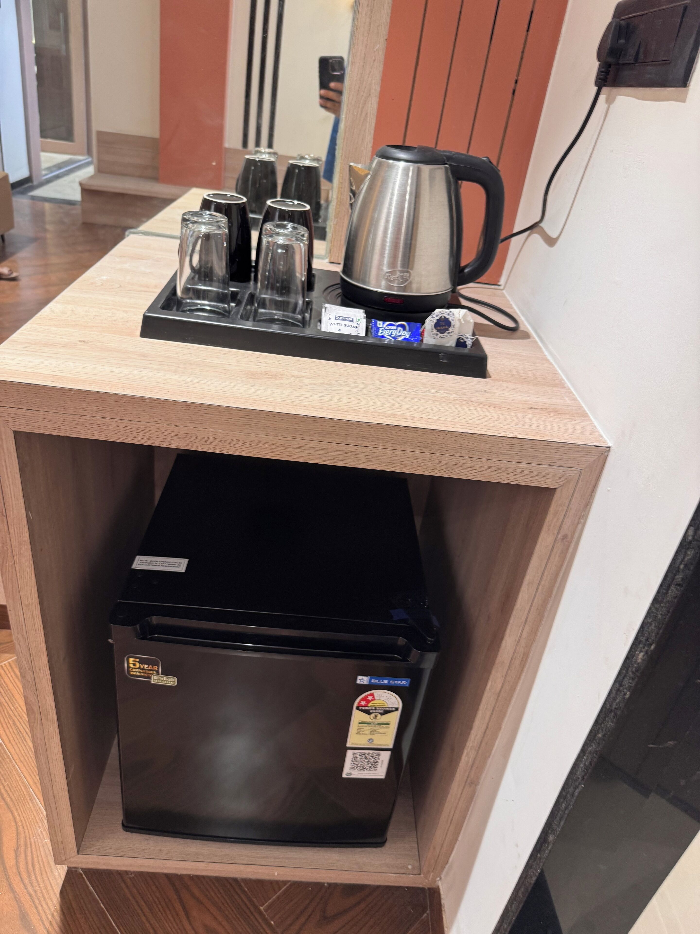 A kitchenette with a stainless steel coffee maker, a black refrigerator, and a tray with glasses and a kettle.