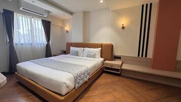 Une chambre d’hôtel avec un grand lit, un plancher en bois, une table de chevet, une lampe fixée au mur et une fenêtre avec des rideaux.
