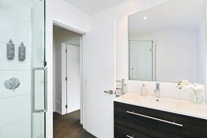 Un baño moderno con cabina de ducha de vidrio, un espejo grande y un mueble de tocador de madera oscura.
