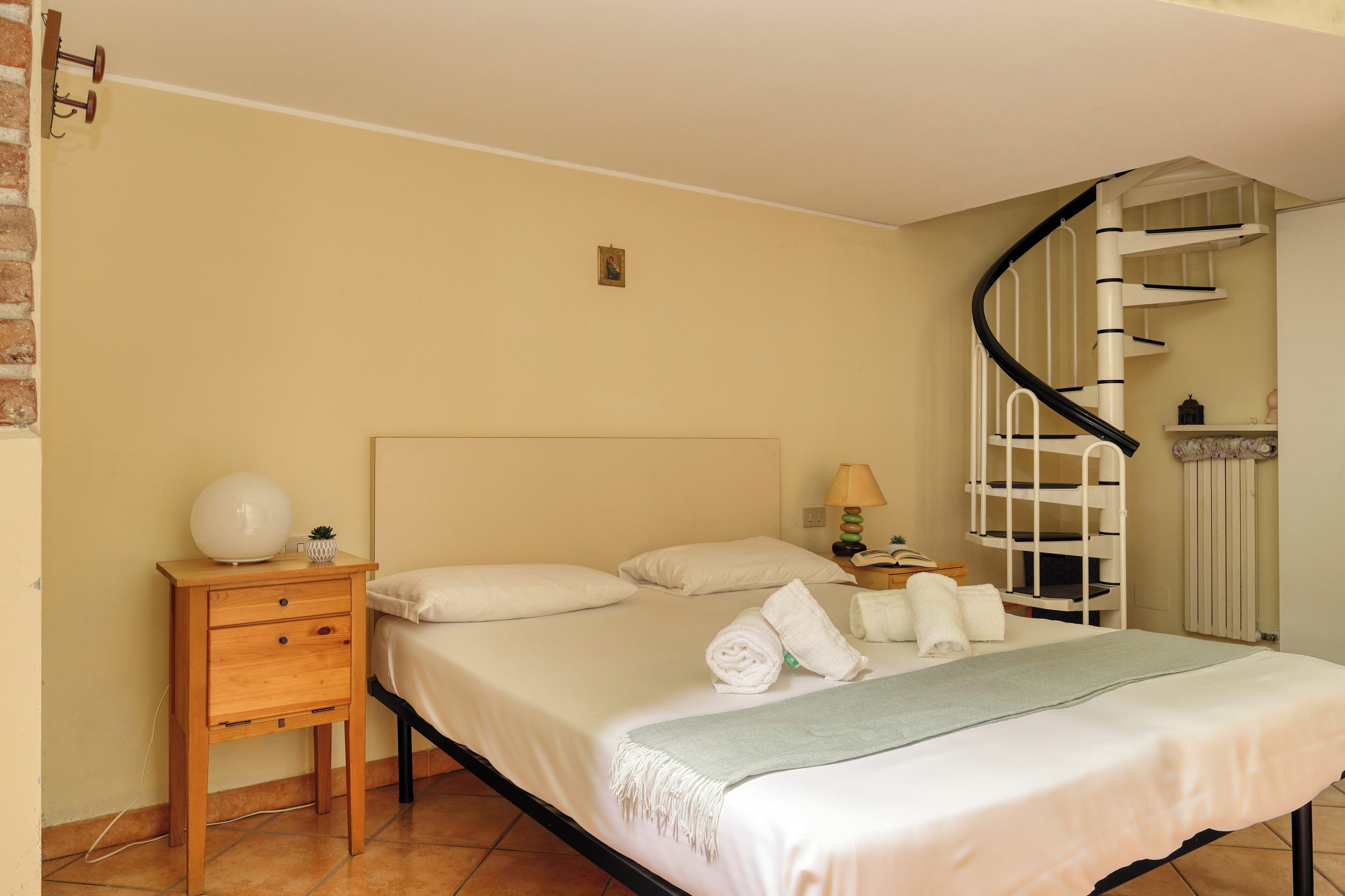 Un dormitorio ordenado con cama, mesitas de noche, una lámpara y una escalera de caracol.