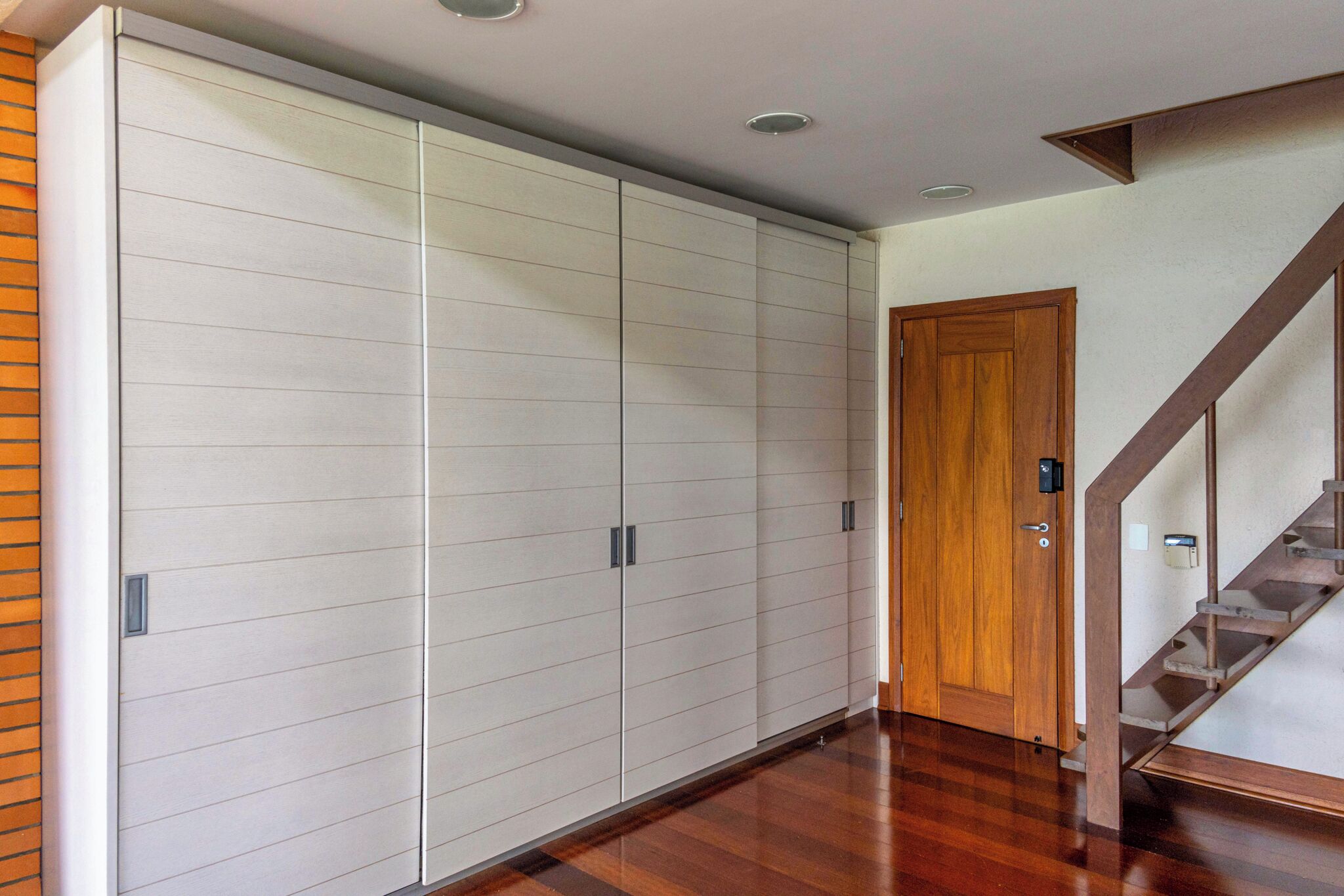 Un pasillo con una escalera de madera, un armario grande y una puerta de madera.
