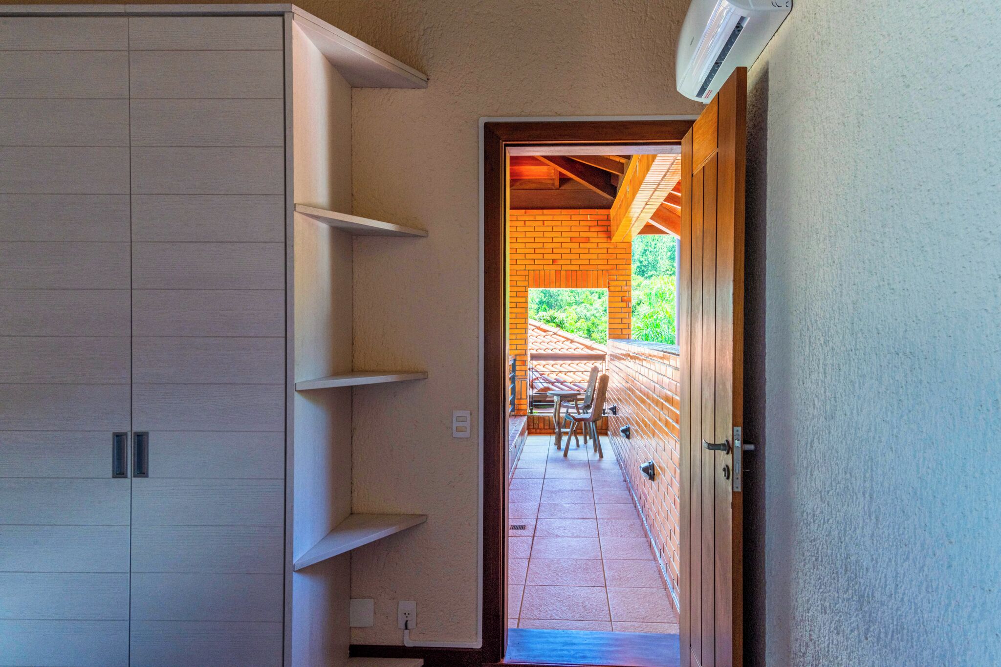 A hallway leading to a patio with a table and chairs, a brick wall, and a wooden door.