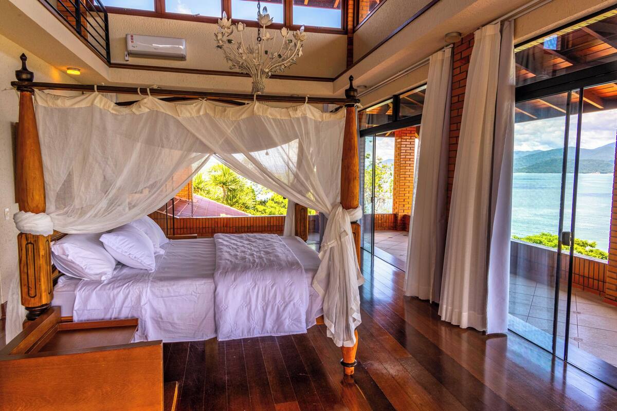 A bedroom with a four-poster bed, a chandelier, and a view of the sea.