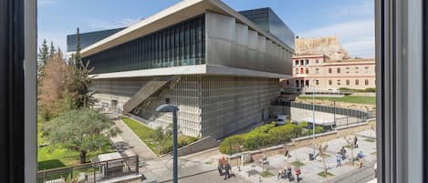 A modern building with a unique angular design, a courtyard with people, and a historic building in the background.