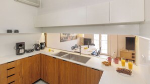 A modern kitchen with a white countertop, wooden cabinets, a double sink, and a dining area with chairs and a table. - Acropolis Museum Retreat by GHH (Athens)