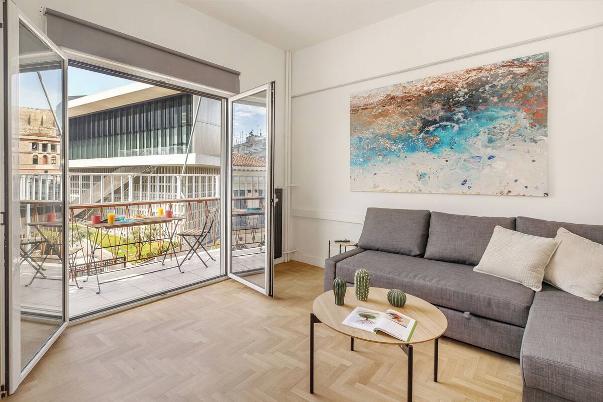 A modern living room with a grey sofa, a coffee table with a magazine, and a large abstract painting on the wall.