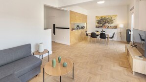 A modern living room with a grey sofa, a wooden coffee table with decorative vases, and a dining area with a wooden herringbone floor. - Acropolis Museum Retreat by GHH (Athens)