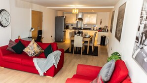 A modern living room with a red sofa, a dining area with a wooden table, and a kitchen with white cabinets and a stainless steel refrigerator. - Apartment Sleeps 6 With Balcony and Parking (Birmingham)