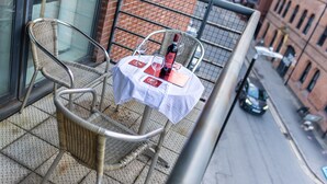 A balcony with wicker chairs, a small table with a bottle and glasses, and a city street view. - Apartment Sleeps 6 With Balcony and Parking (Birmingham)