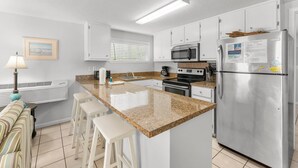 Una cocina moderna con gabinetes blancos, un refrigerador de acero inoxidable, encimera de granito y microondas integrado.