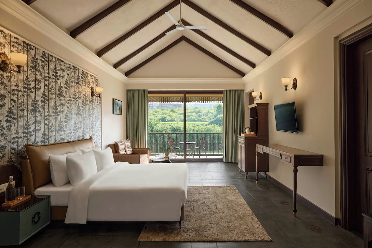 A bedroom with a large bed, a desk, and a balcony with a view.