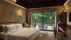 A bedroom with a large bed, a desk, a chair, and a view of the outdoors through a sliding door. - Debu's The Fern Resort & Spa Jim Corbett, Series by Marriott (Ramnagar)