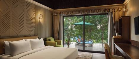 A bedroom with a large bed, a desk, a chair, and a view of the outdoors through a sliding door.