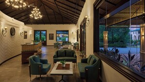 A spacious lobby with a high ceiling, wooden beams, and a large window offering a view of the outdoors. There are several seating areas with green upholstered sofas and a reception desk. - Debu's The Fern Resort & Spa Jim Corbett, Series by Marriott (Ramnagar)
