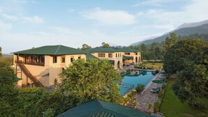 A large building with a swimming pool, surrounded by lush greenery and mountains in the background. - Debu's The Fern Resort & Spa Jim Corbett, Series by Marriott (Ramnagar)