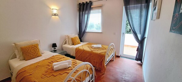 A bedroom with two beds, each with a yellow bedspread and white pillows, a bedside table with a lamp, and a window with curtains. - Charming Carvoeiro villa with private pool, sea view and walk to the beach. (Carvoeiro)