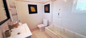 Un baño con lavamanos, inodoro y bañera blancos, y dos cuadros enmarcados en la pared.